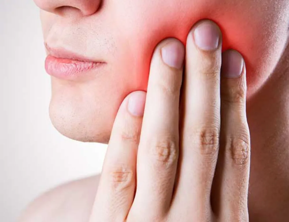 Close-up of a person holding their jaw in pain, indicating jaw discomfort and inflammation, possibly related to severe arthritis or TMJ disorders