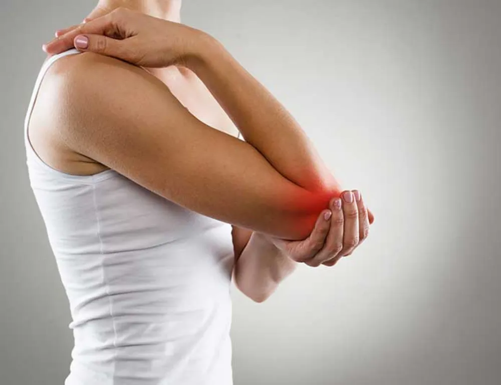 Person holding their elbow in pain, indicating possible symptoms of Rheumatoid Arthritis (RA)