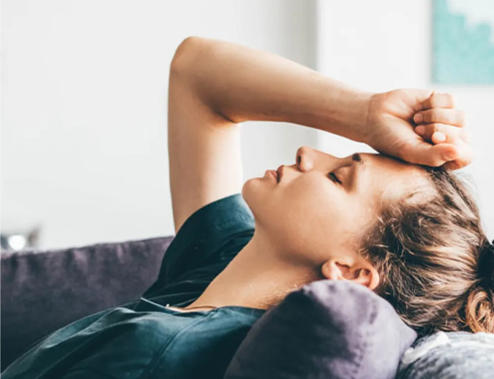 Person lying on a couch with a hand on their forehead, showing signs of fatigue and exhaustion, common in Rheumatoid Arthritis (RA)