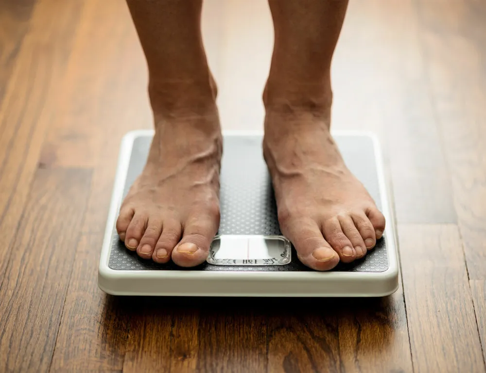 Feet standing on a weighing scale, indicating the importance of weight management for Rheumatoid Arthritis (RA) patients