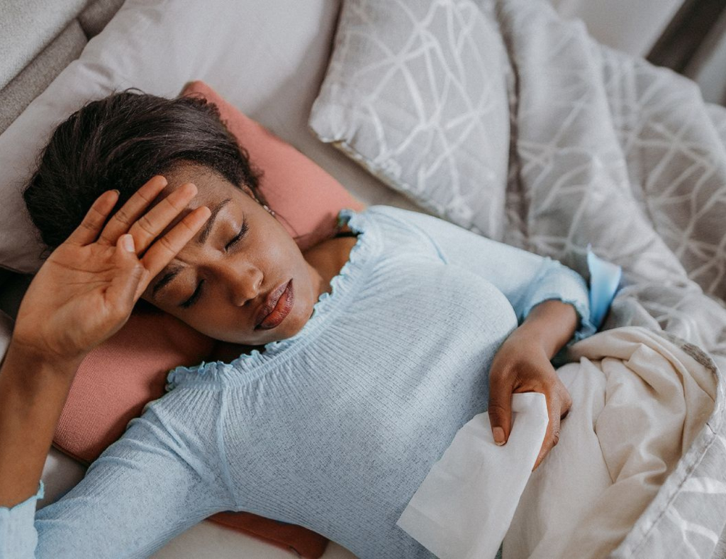 Person lying in bed with a hand on their forehead, indicating fatigue and discomfort, common in Rheumatoid Arthritis (RA) patients